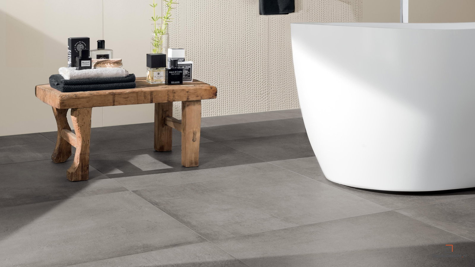 Warme betonlook badkamervloer met houten bankje en wit bad